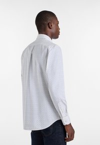 Biała koszula zapinana na guziki z małym, wielokolorowym wzorem kropek, z klasycznym kołnierzykiem i długimi rękawami, wykonana z gładkiego materiału.