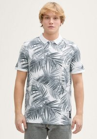 Koszulka polo z krótkim rękawem w kolorze białym z czarnym wzorem liści palmowych, z kołnierzykiem i listwą z guzikami, wykonana z lekkiego materiału.