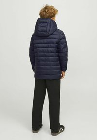 Námornícka puffer bunda s kapucňou, s prešívaným dizajnom, na zips a elastickými manžetami. V kombinácii s čiernymi nohavicami a čiernou obuvou.