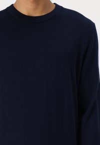 Tamsiai mėlynas ilgos rankovės megztinis su apvaliu iškirpimu, turintis minkštą tekstūrą ir laisvą siluetą. Be siūlių pečių dizainas.