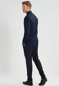 Marineblå skjorte med lange ermer og mørke bukser, glatt tekstur, tettsittende design, elegant silhuett, kombinert med svarte sko, minimalistisk stil.