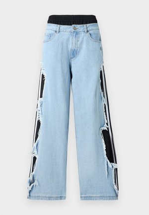 Világoskék farmernadrág fekete elasztikus derékpánttal, kopott oldalakkal, melyek fekete-fehér csíkos anyagpanelekre engednek betekintést alatta.