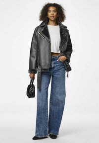 Giubbotto di pelle nera con fodera in pelliccia sintetica grigia, top leggero grigio chiaro cropped, jeans blu a gamba larga e piccola borsa nera. La modella sta in piedi.