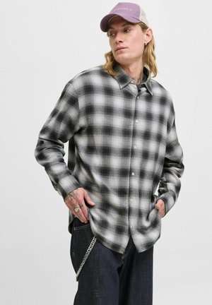 Camisa de franela a cuadros en gris y blanco con botones en el frente y mangas largas, combinada con jeans oscuros y una gorra morada.