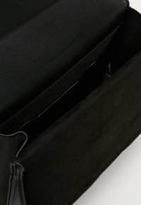 Wnętrze czarnej torebki z zamszu i skóry o gładkiej fakturze, z otwartą komorą i minimalistycznym designie, bez widocznych elementów metalowych.