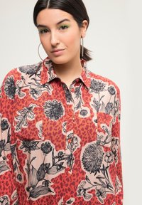Camicia button-up a fantasia floreale caratterizzata da una combinazione di rosso e rosa chiaro, con contorni neri, maniche lunghe e una tasca sul petto.
