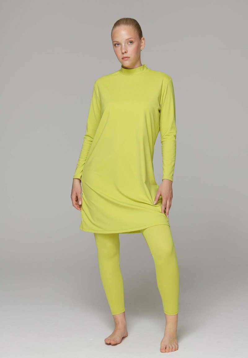Limoengroene sportoutfit bestaande uit een hoge nek lange mouwen tuniek en bijpassende legging, gemaakt van gladde, rekbare stof.