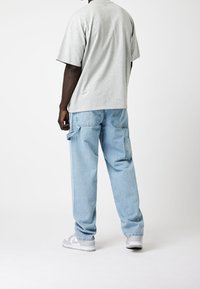 Harmaa ylisuuri t-paita, vaaleansiniset väljät farkut sivutaskuilla ja harmaat lenkkarit valkoisilla yksityiskohdilla. Minimalistinen muotoilu ja rento istuvuus.