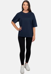 T-shirt en coton bleu marine à manches courtes, col rond, coupe décontractée, associé à des leggings noirs et des baskets blanches.