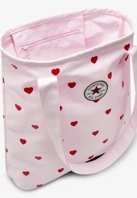 Ροζ υφασμάτινη τσάντα ώμου με κόκκινο μοτίβο καρδιάς, εξωτερική θήκη, και λογότυπο Converse All Star. Ανθεκτικοί, φαρδιοί ιμάντες ώμου.