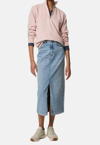 Lichtroze sweatvest met rits en blauwe denim midi-rok met een split aan de voorkant. Gecombineerd met beige sportschoenen.