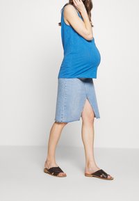 Modrá bezrukávová halenka, světle modrá džínsová sukně s předním rozparkem, roztrhaným lemem a hnědými plochými sandály. Sukně sahá nad kolena, má ležérní design.