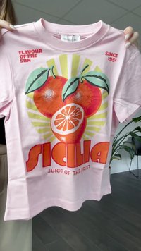 Lyserød kortærmet t-shirt med iøjnefaldende orange grafikker, herunder appelsiner og teksten "SICILIA JUICE OF THE FRUIT" i livlige farver.