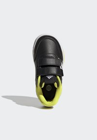 Zapatilla negra con acabado texturizado, interior amarillo y dobles correas de velcro. Presenta una suela de goma blanca y el logo de Adidas en la lengüeta.