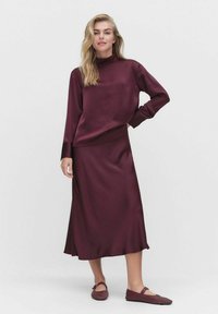 Burgundy satin tvådelad outfit bestående av en långärmad, höghalshöjd topp och en matchande ankel-lång kjol, kombinerad med texturerade burgundy lägenheter.