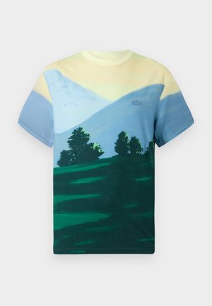 T-shirt à manches courtes arborant un dégradé de jaune clair et de bleu en haut, avec un paysage vert et des arbres imprimés dans la partie inférieure.