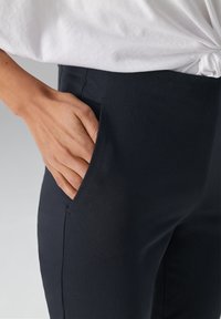 Donkerblauwe broek met een zijzak en een gestructureerde stofafwerking, gecombineerd met een licht, geknoopt wit topje.