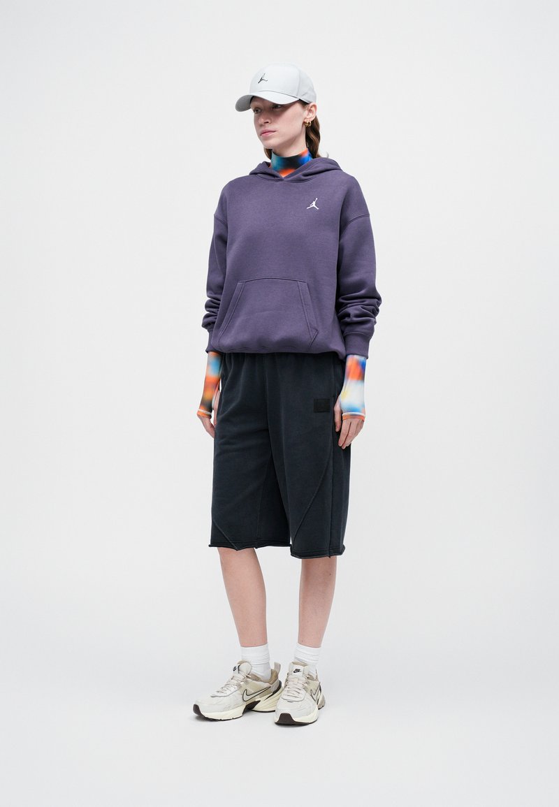 Paarse hoodie met een voorkraag, zwarte knielange shorts en een lichtgrijze pet. Witte en beige sneakers met accenten op de tussenzool.