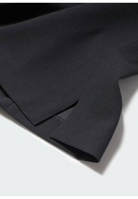 Gros plan sur un tissu noir avec un détail de ourlet en couches mettant en avant la texture et les coutures soignées sur un fond clair.