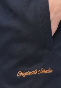 Tengerészkék pamut pulóver narancssárga "Originals Studio" hímzéssel. Oldalzsebbel és texturált kötött mintával.