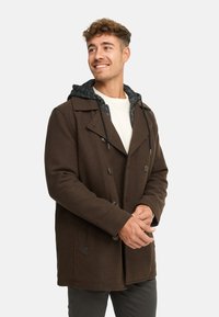 Cappotto marrone in misto lana con design doppiopetto, grandi bottoni e cappuccio foderato in pile grigio. Presenta tasche laterali e una vestibilità sartoriale.