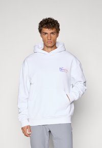 White cotton hoodie with a front pocket, drawstring hood, and printed logo in purple and orange. Ribbed cuffs and hem. Soft texture.