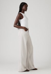 Bež široke hlače od mekanog, teksturiranog materijala, uparene s uskim bijelim majicama bez rukava. Hlače imaju bočne džepove i ležeran kroj.