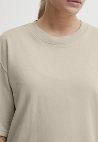 Beige bomulls sweatshirt med ribbat rundhals och korta ärmar. Tygets textur är slät med en något elastisk kvalitet.