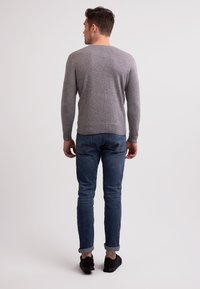 Grauer Pullover aus weichem Material, taillierte Passform, runder Halsausschnitt, getragen über blauen Jeans, hochgekrempelte Ärmel und schwarze Sneakers.