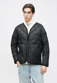 Melnā krāsā šūts jaka ar V veida kakla izgriezumu, rāvējslēdzēja aizdari un garām piedurknēm, valkāta virs baltas augstas kakla blūzes. Mīksts, viegls audums.