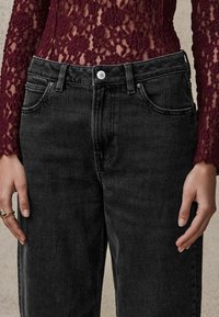 Jean en denim noir taille haute avec une coupe droite, comportant cinq poches, une fermeture à bouton à l'avant et une texture légèrement délavée.