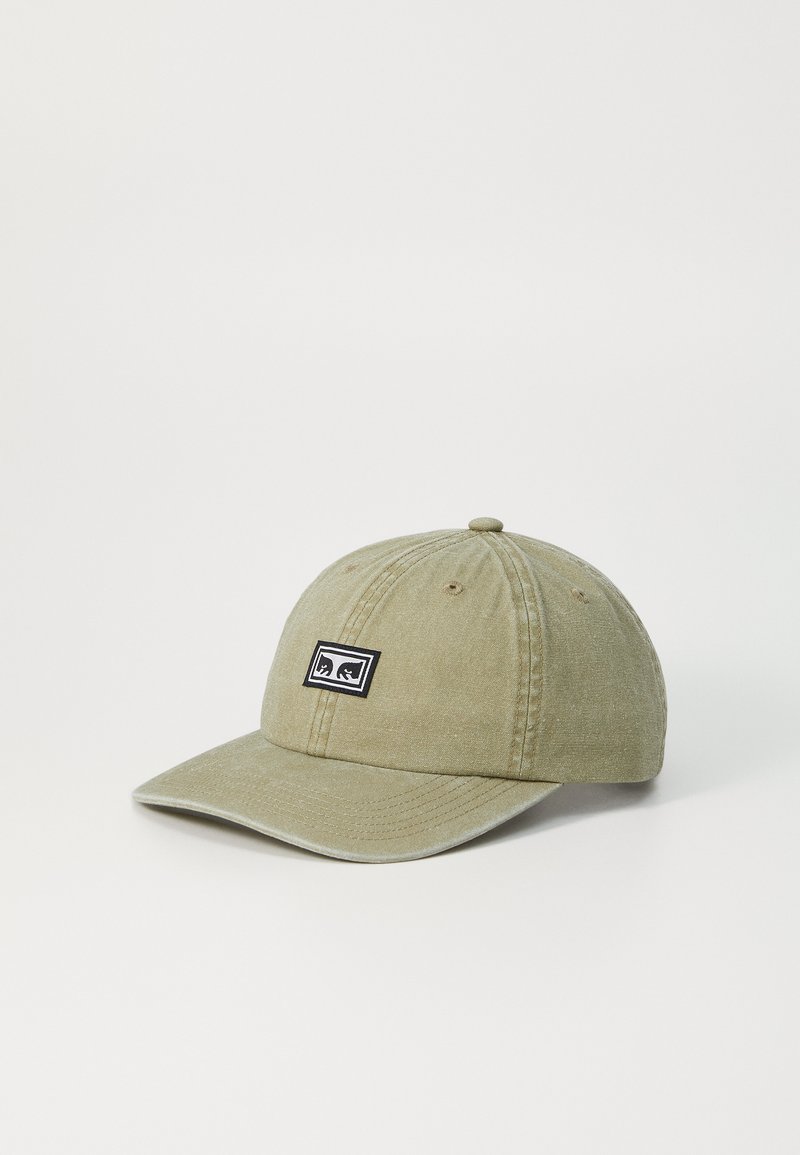 Khaki baseball caps med buet skjerm, teksturert stoff og en svart rektangulær logo-patch med to stiliserte figurer på forsiden.