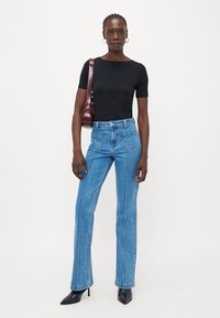 Svart kortermet topp kombinert med blå høy midje flared jeans. Jeansene har en ren skåret og synlig sømdetalj, supplert med svarte hæler.
