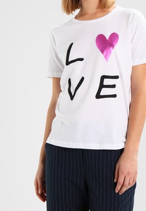 Camiseta de algodón blanca con grandes letras negras que dicen "LVE" y un gráfico de un corazón rosa. Mangas cortas y corte relajado.