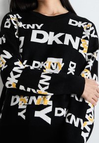 Svart stickad tröja med ett upprepat DKNY-logomönster i vitt och gult. Rund halsringning med ribbade muddar och fåll.