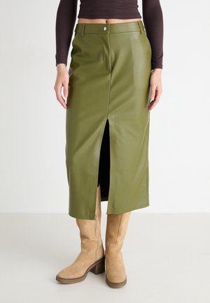 Midi-nederdel i olivengrønt læder med frontslids, båret med lysebrune ruskind knæhøje støvler og mørk langærmet croptop.