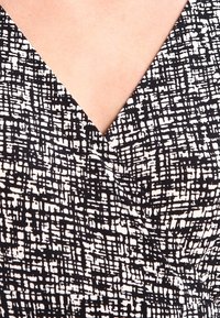 Svartvitt mönstrad klänning med V-ringning. Tyget har abstrakta linjetexturer mot en ljus bakgrund.