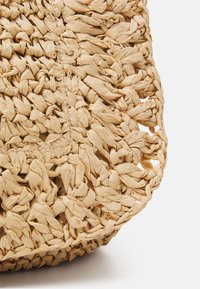Borsa in paglia intrecciata di un beige chiaro con superficie testurizzata, che presenta motivi intricati e un design a tessitura aperta lungo i bordi.
