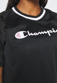 Black mesh short-sleeve shirt with a rounded collar. Features white "Champion" logo across the chest and subtle perforated texture.