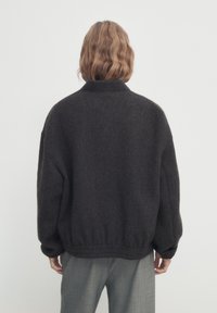Veste oversize gris foncé en tissu doux et texturé, avec un col et une taille élastiquée. Le dos présente un design simple.