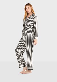 Zwart-wit gestreept pyjamapak met lange mouwen, knoopsluiting aan de voorkant en elastische tailleband. Zacht materiaal met contrasterende manchetten en kraag.