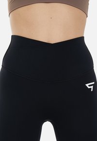 Höga svarta leggings med en mjuk yta, med en överlappande design vid midjan och en vit logotyp på vänster höft.