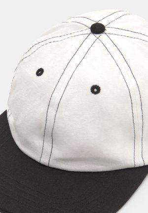 Bijela kapa s crnim vizirjem, s kontrastnim crnim šavovima, okruglom krunom i ventilacijskim otvorima. Mjereno teksturirani gornji sloj tkanine.