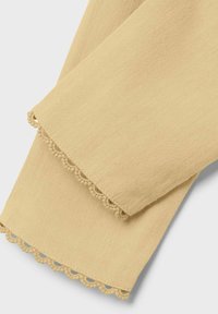 Jasnożółty materiał o teksturowanej powierzchni; na krawędzi znajduje się falbanka z koronką. Prosty wzór, miękka i gładka faktura.