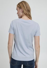 Camiseta de manga corta azul claro con cuello redondo y un corte relajado; hecha de una tela suave con una ligera textura. La vista trasera muestra un diseño minimalista.
