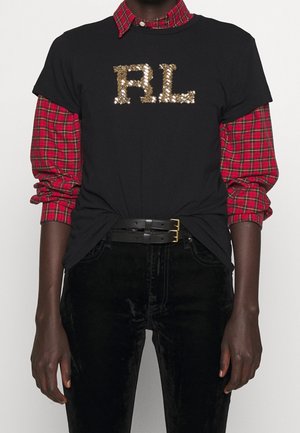 Person wearing black T-shirt with gold sequined "RL" letters over red plaid long-sleeve shirt, black belt, and black pants.