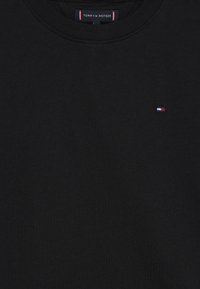 T-shirt preta de gola redonda com pequeno logotipo da bandeira Tommy Hilfiger no peito e etiqueta da marca dentro da gola.