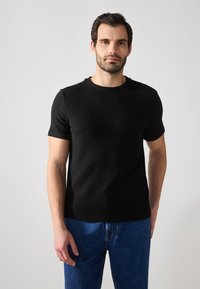 T-shirt nera a maniche corte con collo rotondo, abbinata a jeans in denim blu. Il tessuto ha un aspetto texturizzato.