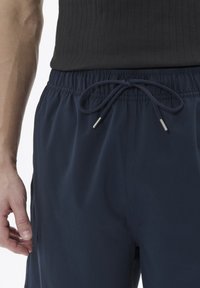 Jūros mėlynų spalvos kelnės su užtraukiama juosta ir metalinėmis detalėmis, turinčios lygią tekstūrą ir elastinę juosmenį patogumui.