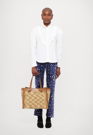 Blusa bianca con parte anteriore arricciata, pantaloni blu con motivo e borsa a tracolla intrecciata marrone. Le scarpe con tacco nere completano l'outfit.